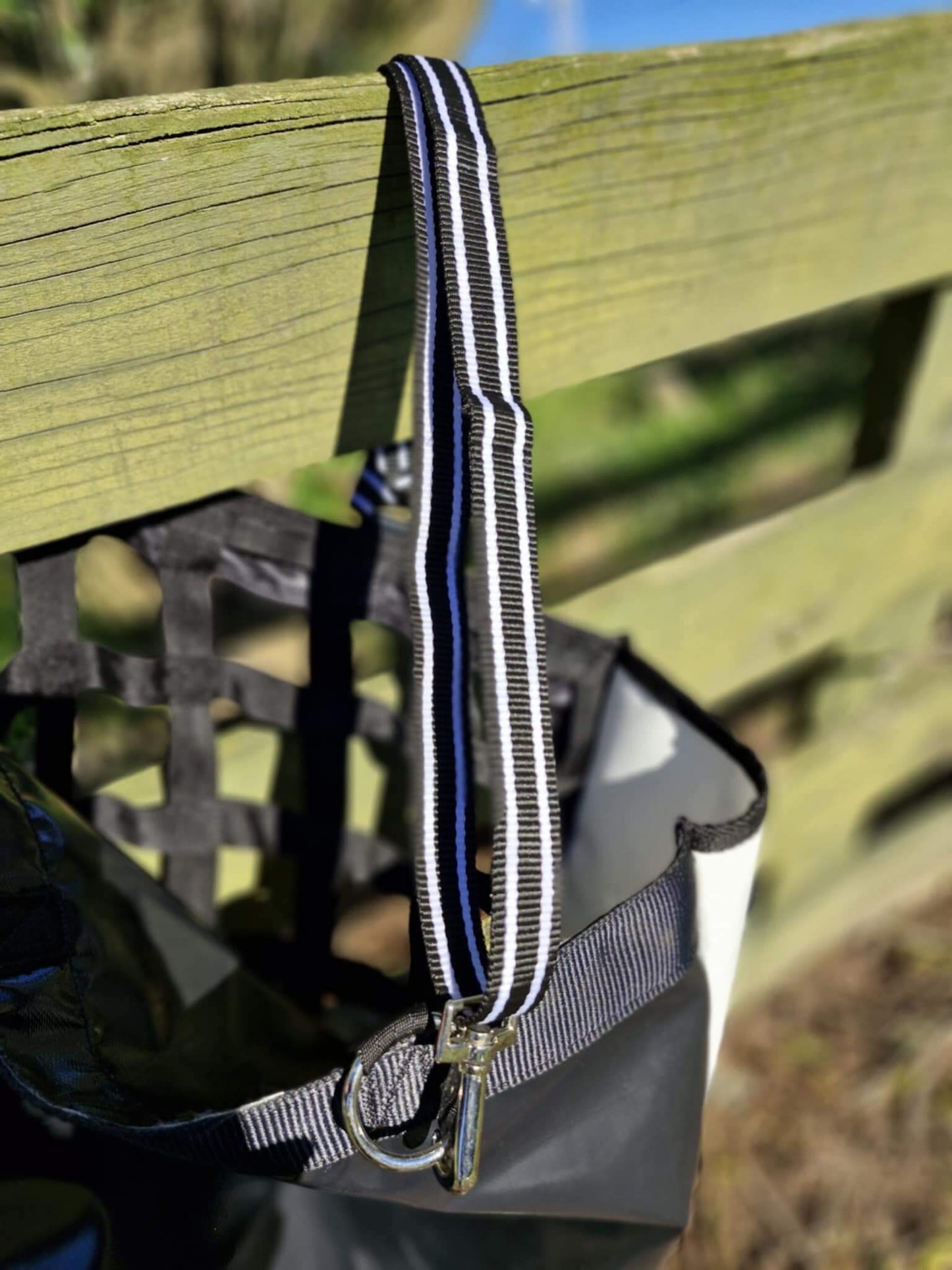 Close-up of FCR Slow Feed Haybag strap with clip hanging on a wooden fence, showcasing stylish design and durability.
