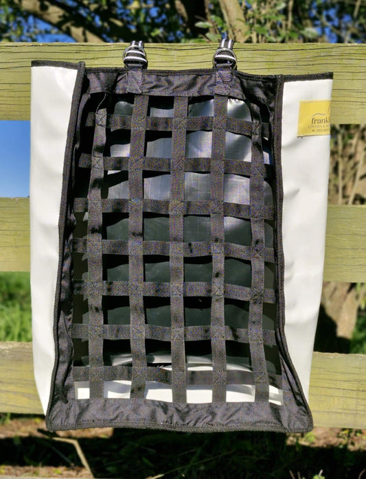 FCR Slow Feed Haybag hanging on a fence, designed to promote natural foraging and reduce hay waste.